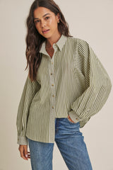 woman wearing a green and white striped oversized button-up shirt with rolled sleeves and light blue jeans