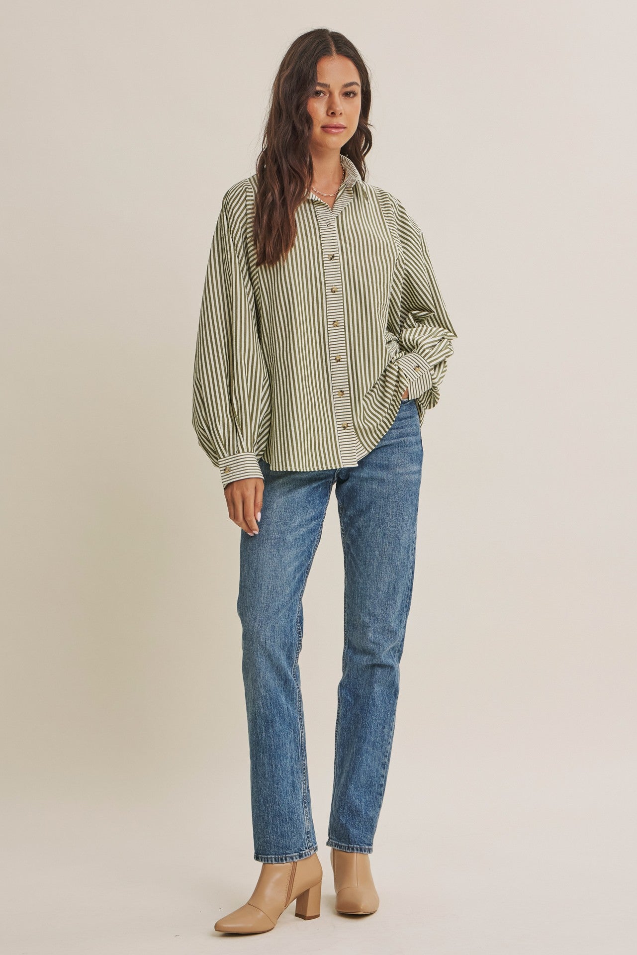 woman wearing a green and white striped oversized button-up shirt with balloon sleeves and blue jeans