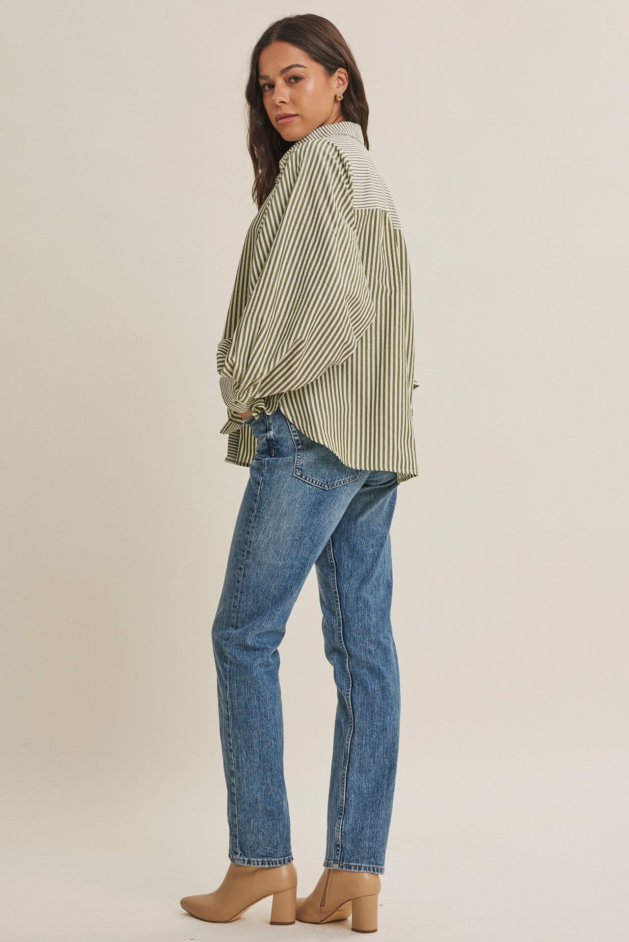woman wearing a green and white striped oversized shirt with balloon sleeves and blue jeans, standing sideways