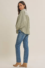 woman wearing a green and white striped oversized shirt with balloon sleeves and blue jeans, standing sideways