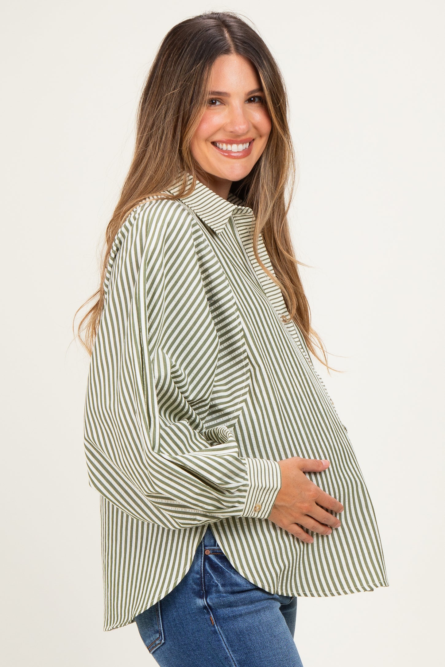 woman wearing a green and white striped maternity button-up shirt and holding her baby bump