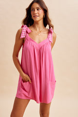 woman wearing a bright pink sleeveless dress with gingham tie straps and front pockets