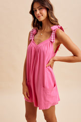 woman wearing a pink sleeveless dress with gingham tie straps and front pockets