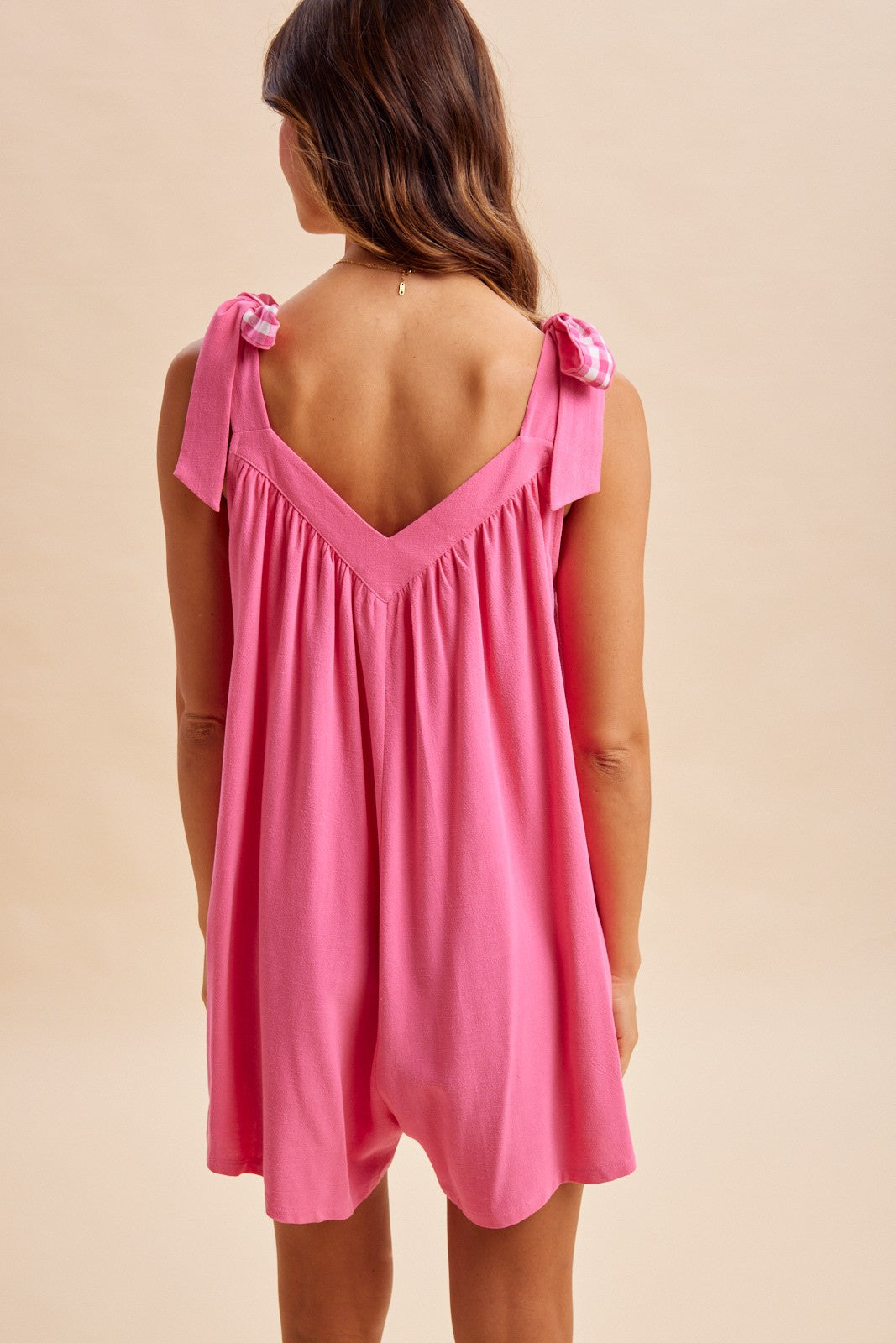 woman wearing a pink sleeveless romper with bow tie straps and a relaxed fit from the back