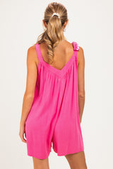 woman wearing a bright pink sleeveless maternity romper with a gathered back and checkered strap detail