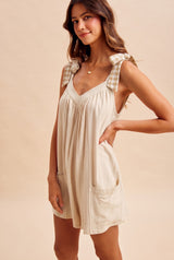 woman wearing a beige sleeveless dress with plaid tie straps and front pockets