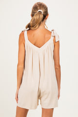 woman wearing a beige maternity romper with tied shoulder straps and a gathered back design