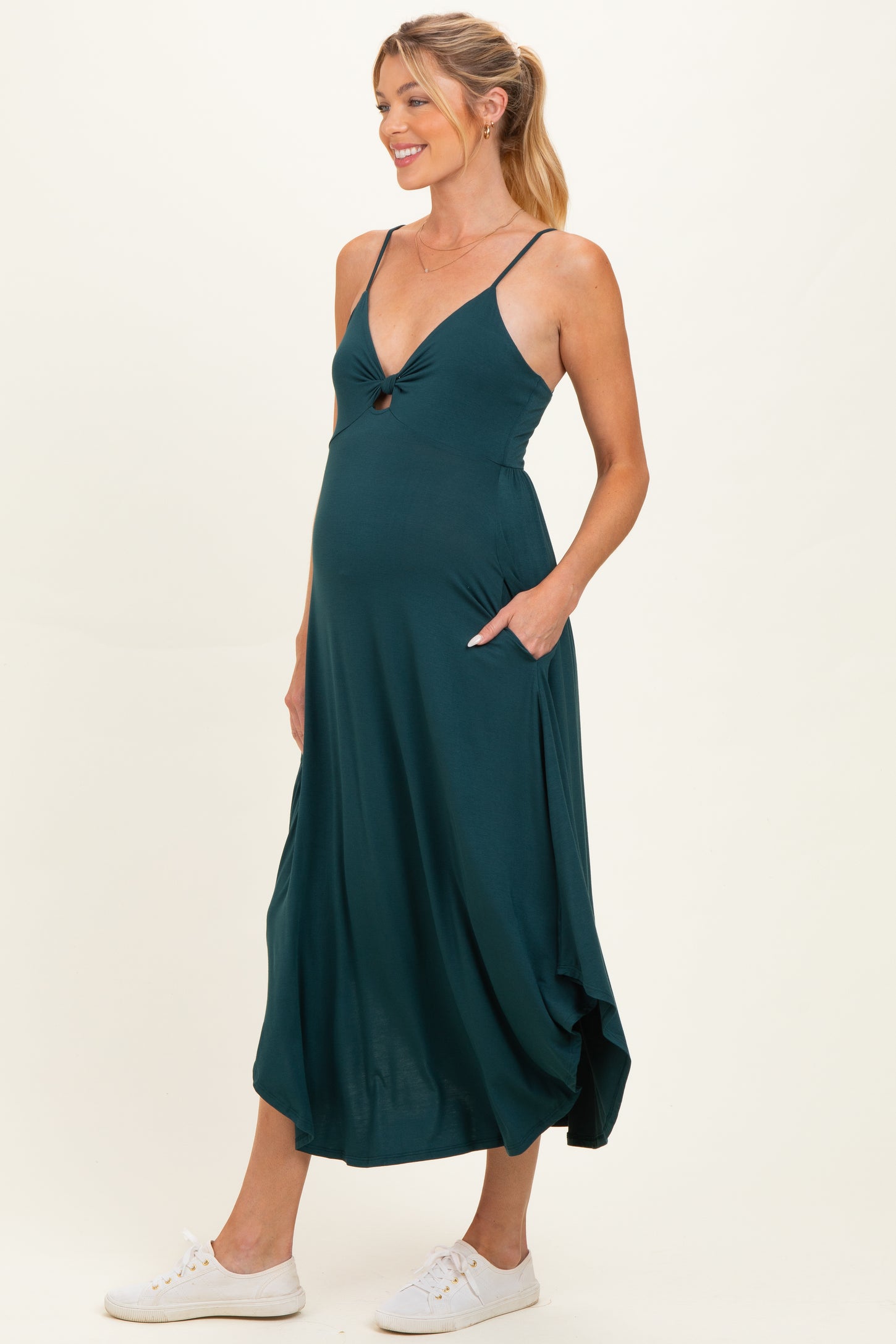 woman wearing a teal maternity dress with a front knot detail and pockets, showcasing her baby bump
