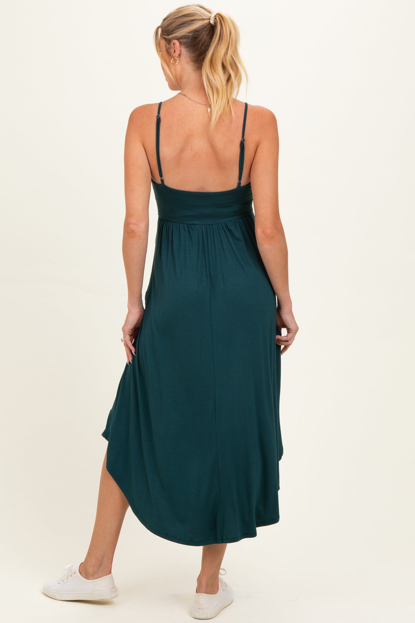 woman wearing a dark teal maternity maxi dress with adjustable straps and a flowing hem, showing her baby bump