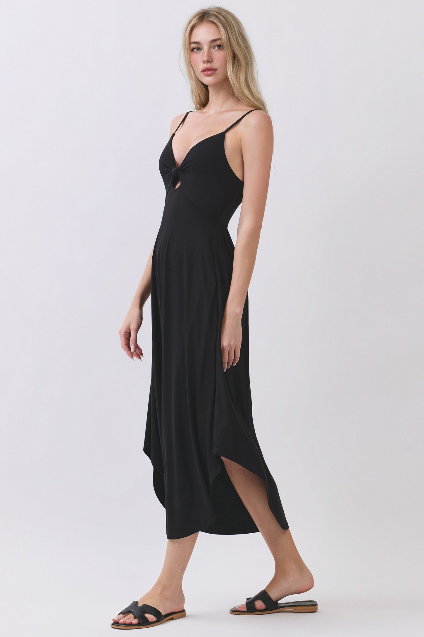 woman wearing a black maxi dress with a cutout detail and spaghetti straps, styled with flat sandals