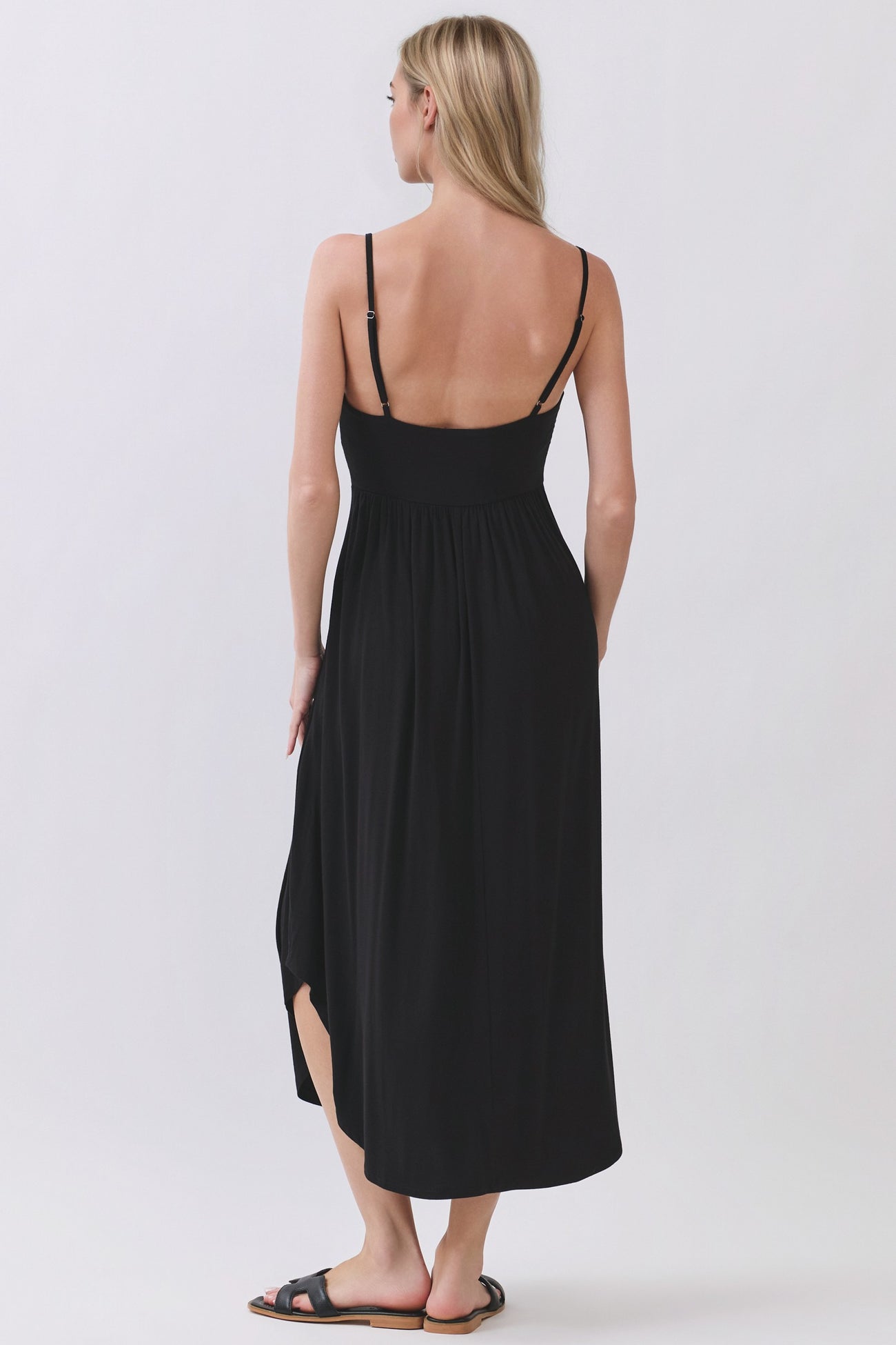 woman wearing a black maxi dress with adjustable straps and a side slit, shown from the back