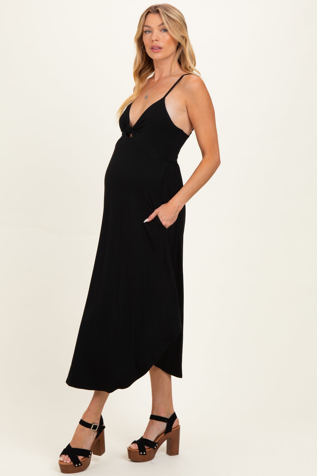 woman wearing a black sleeveless maternity dress with a knot detail and pockets, showcasing her baby bump