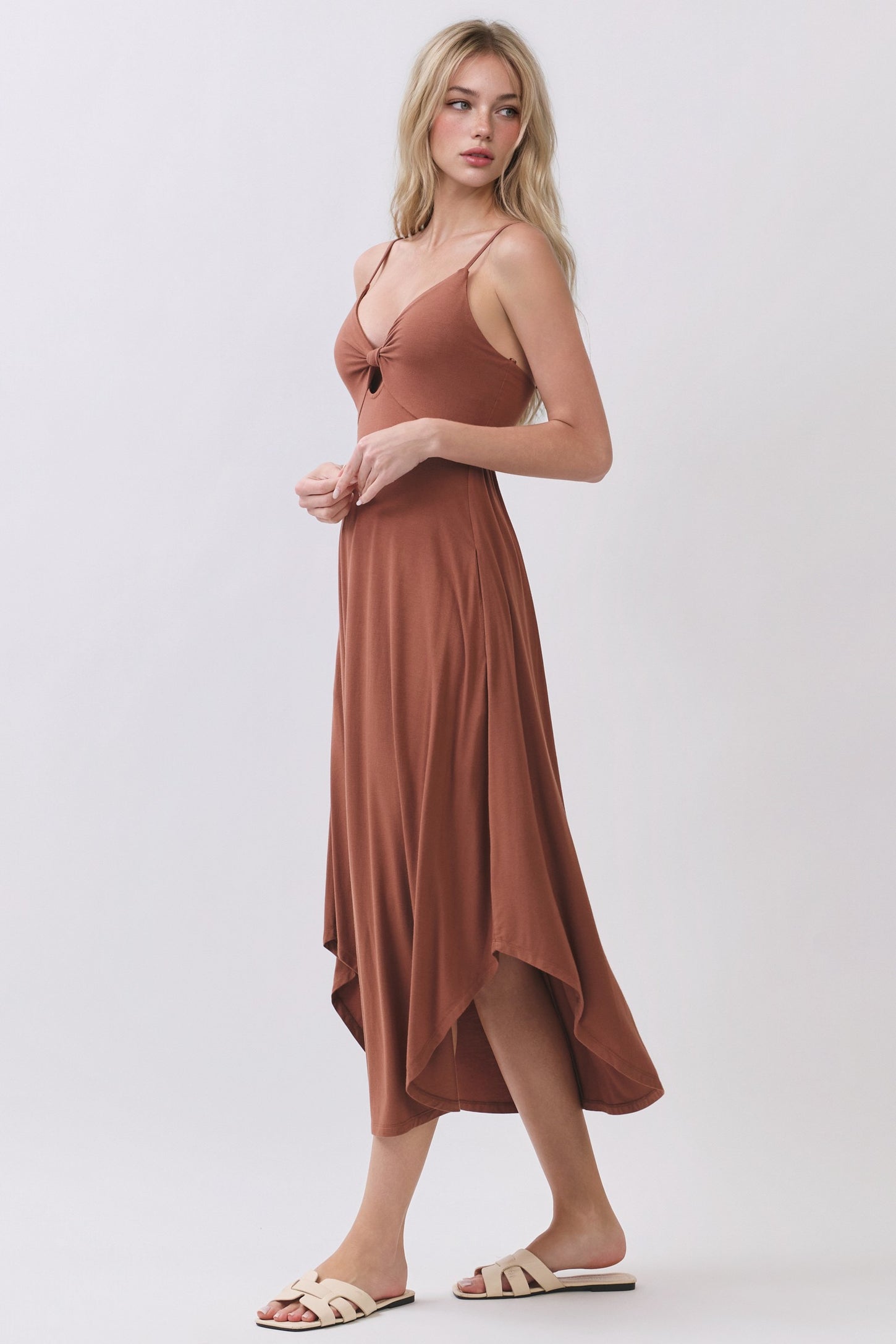 woman wearing a brown spaghetti strap midi dress with a twist front detail and a high-low hemline