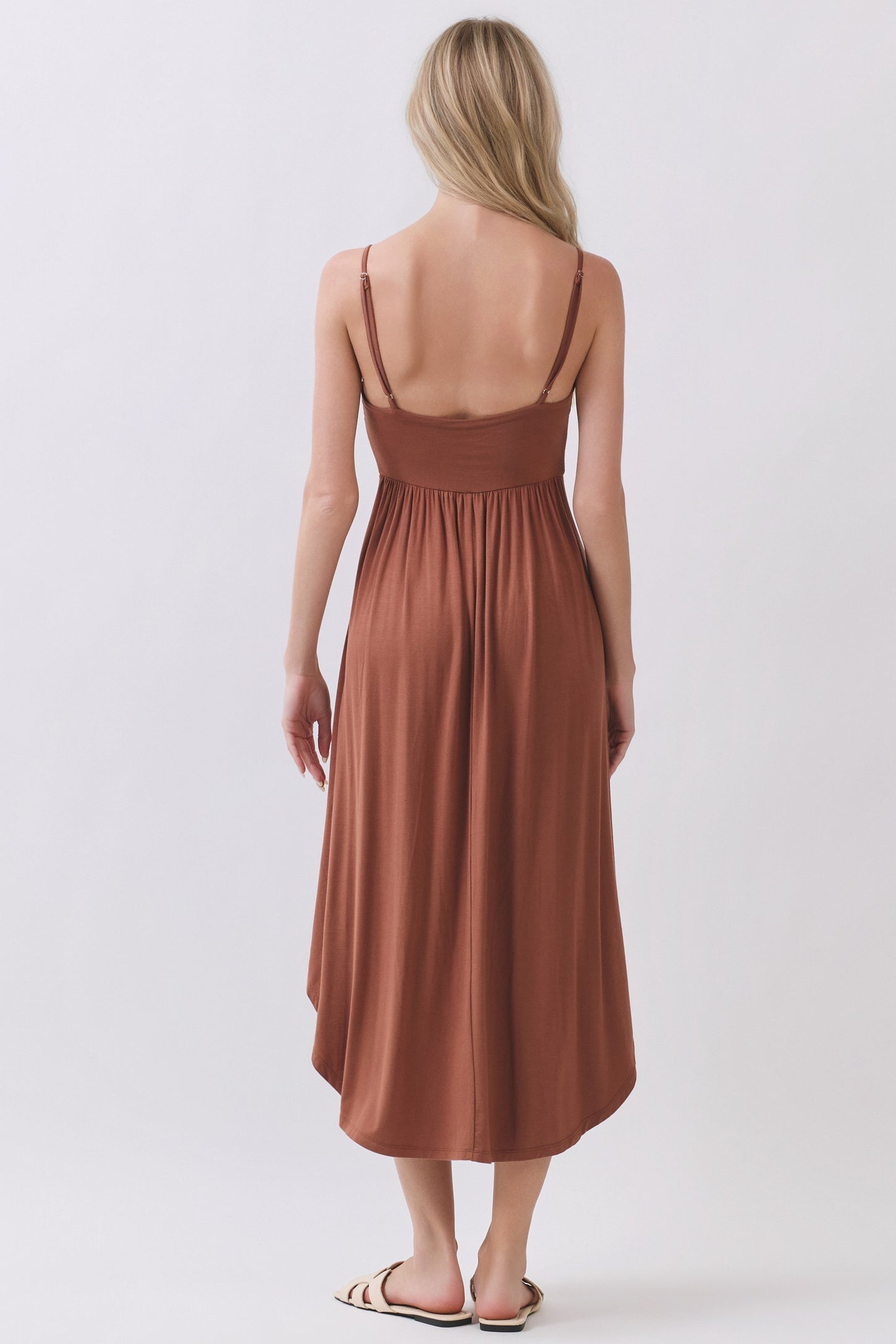 woman wearing a brown sleeveless maxi dress with a cinched waist and a flowy skirt, seen from the back