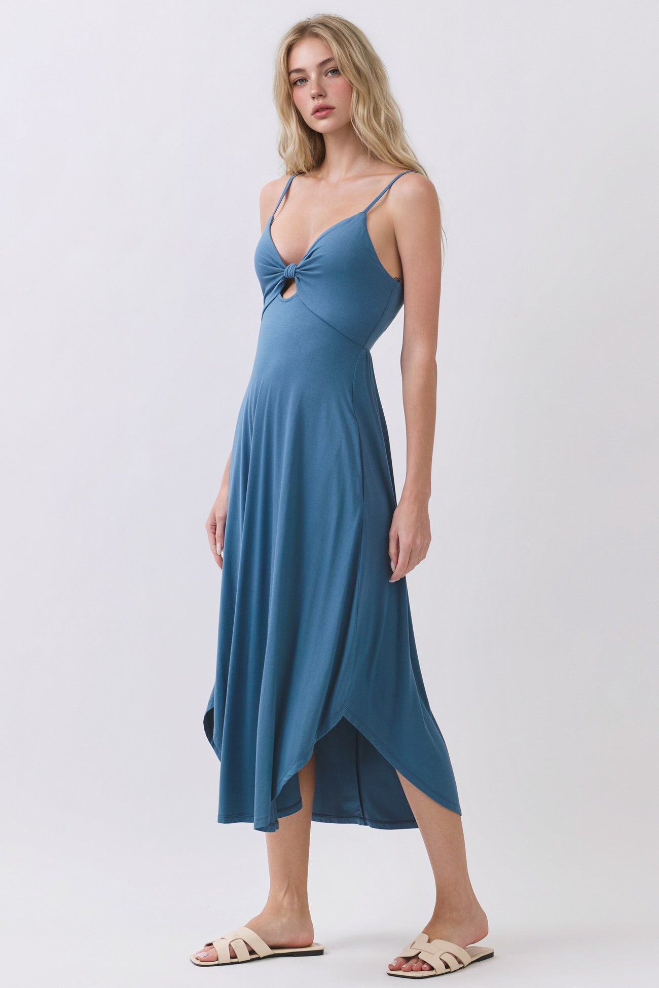 woman wearing a blue spaghetti strap midi dress with a front knot detail and an asymmetrical hemline