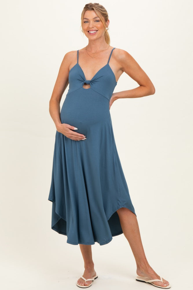 woman wearing a blue maternity dress with a knot detail and high-low hem, posing with her baby bump visible