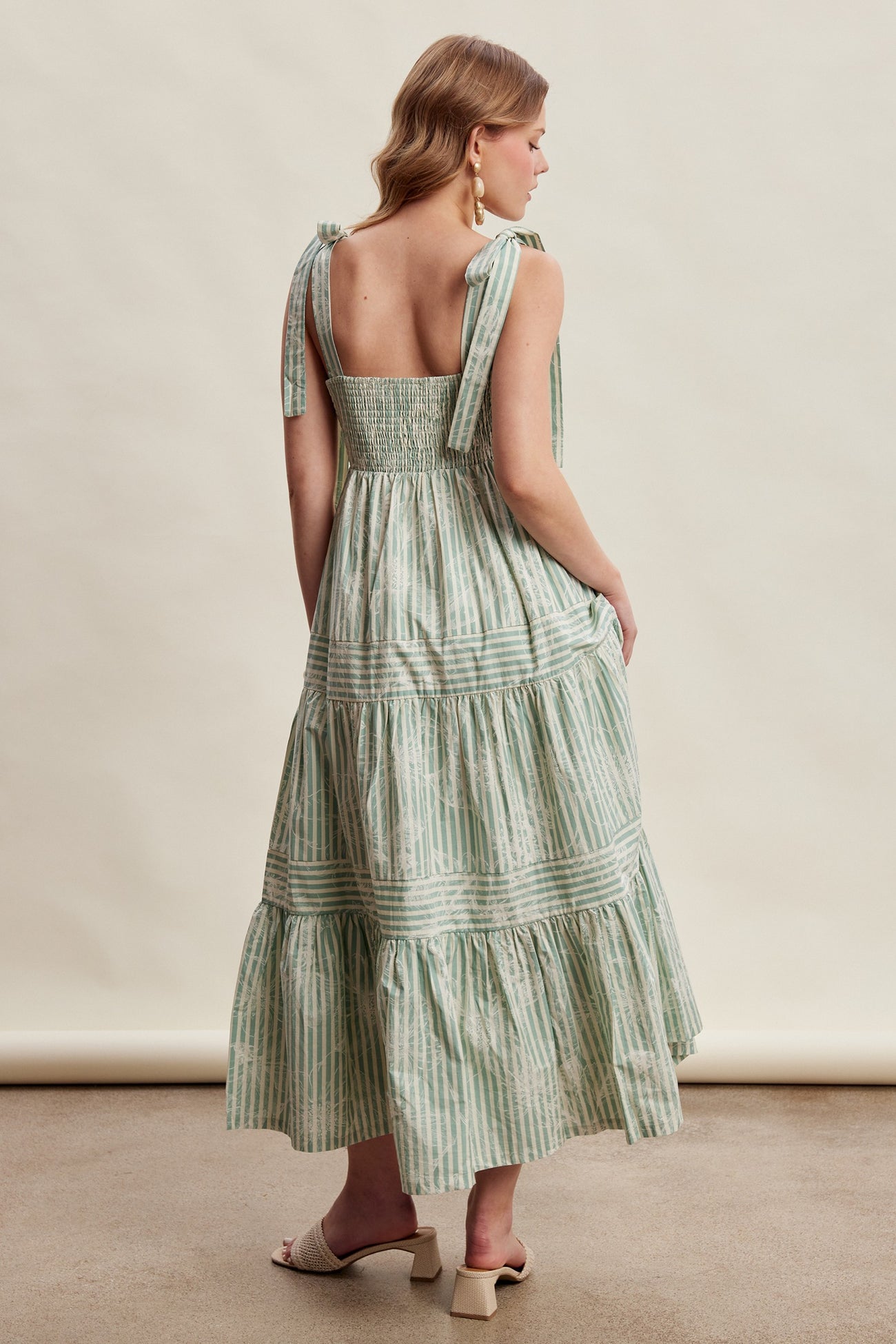 woman wearing a green and white striped maxi dress with tie straps and a smocked back, seen from the back