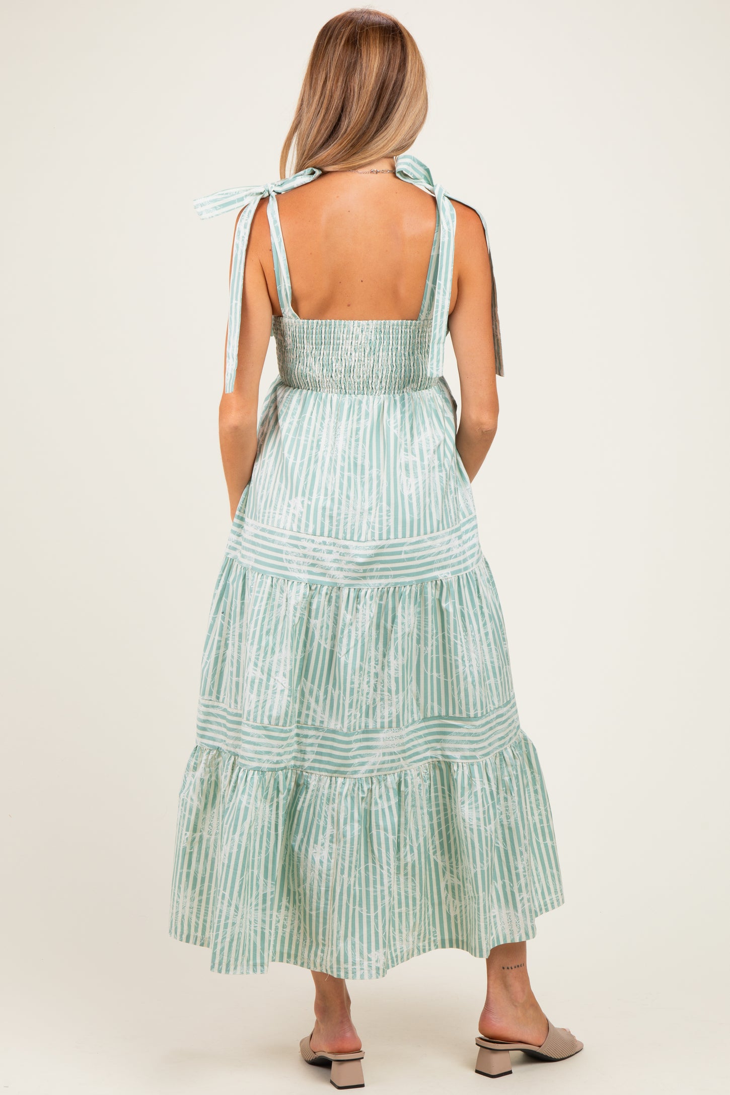 woman wearing a light green striped maternity maxi dress with a smocked back and tie straps