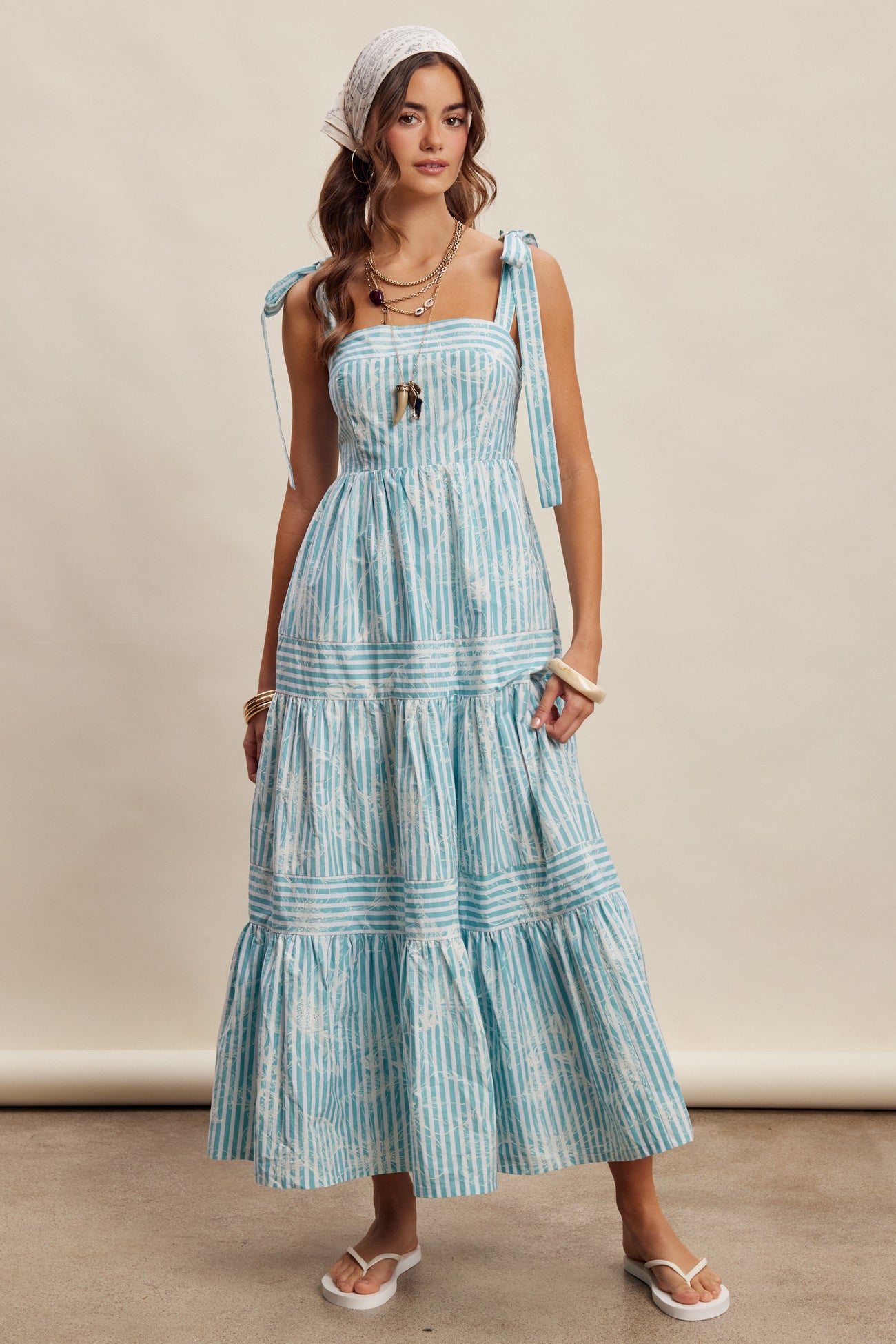 woman wearing a blue and white striped maxi dress with tie straps and a tiered skirt, styled with accessories and sandals