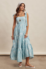 woman wearing a light blue striped sundress with tie straps and tiered skirt, accessorized with a white headband and jewelry