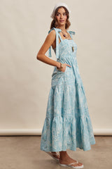 woman wearing a light blue striped maxi dress with tie straps and pockets, standing sideways with a headscarf and sandals