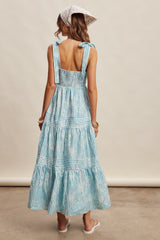 woman wearing a light blue tie-dye maxi dress with smocked back and shoulder ties, standing with her back to the camera