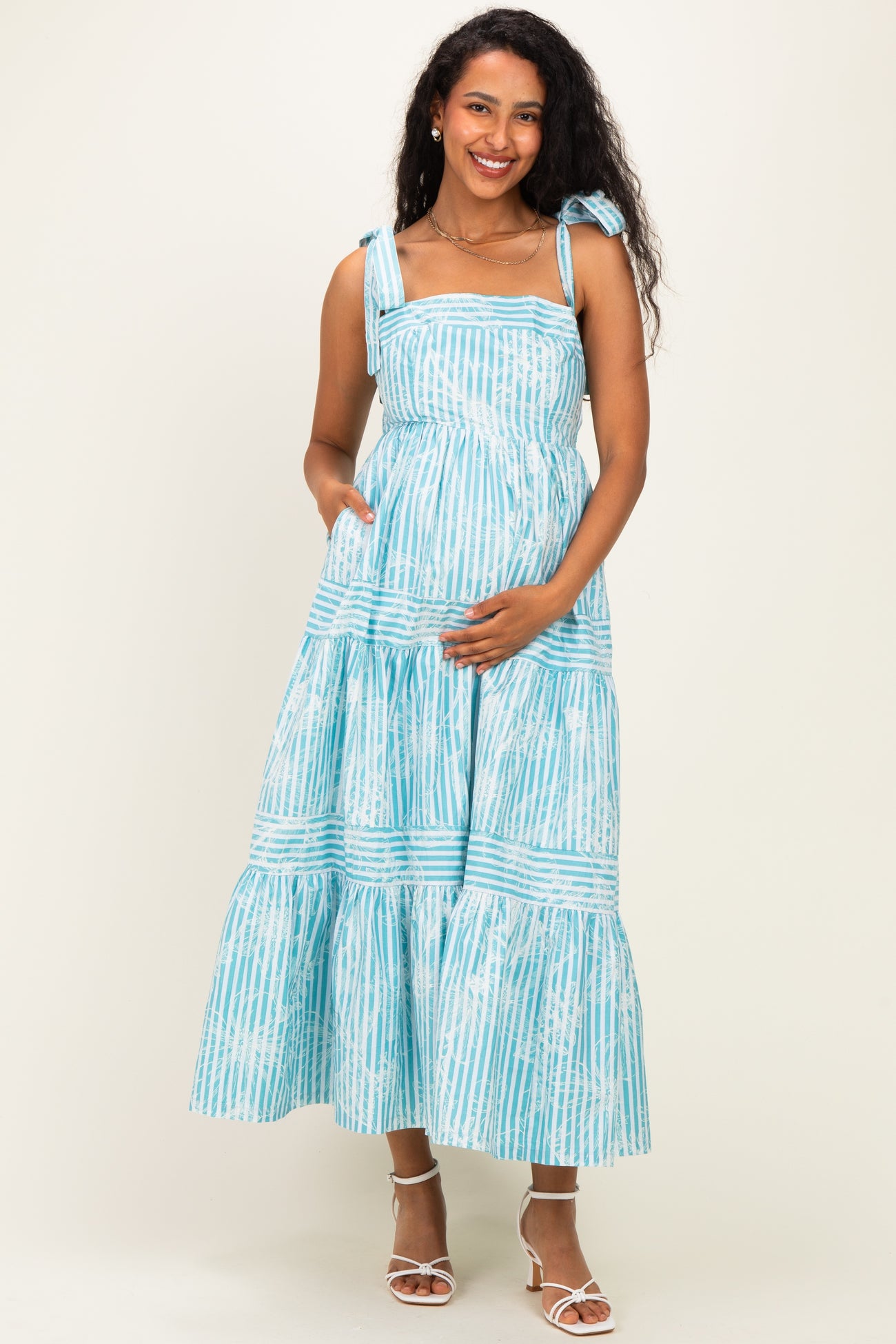 woman wearing a light blue maternity maxi dress with tie straps and a tiered skirt, holding her baby bump