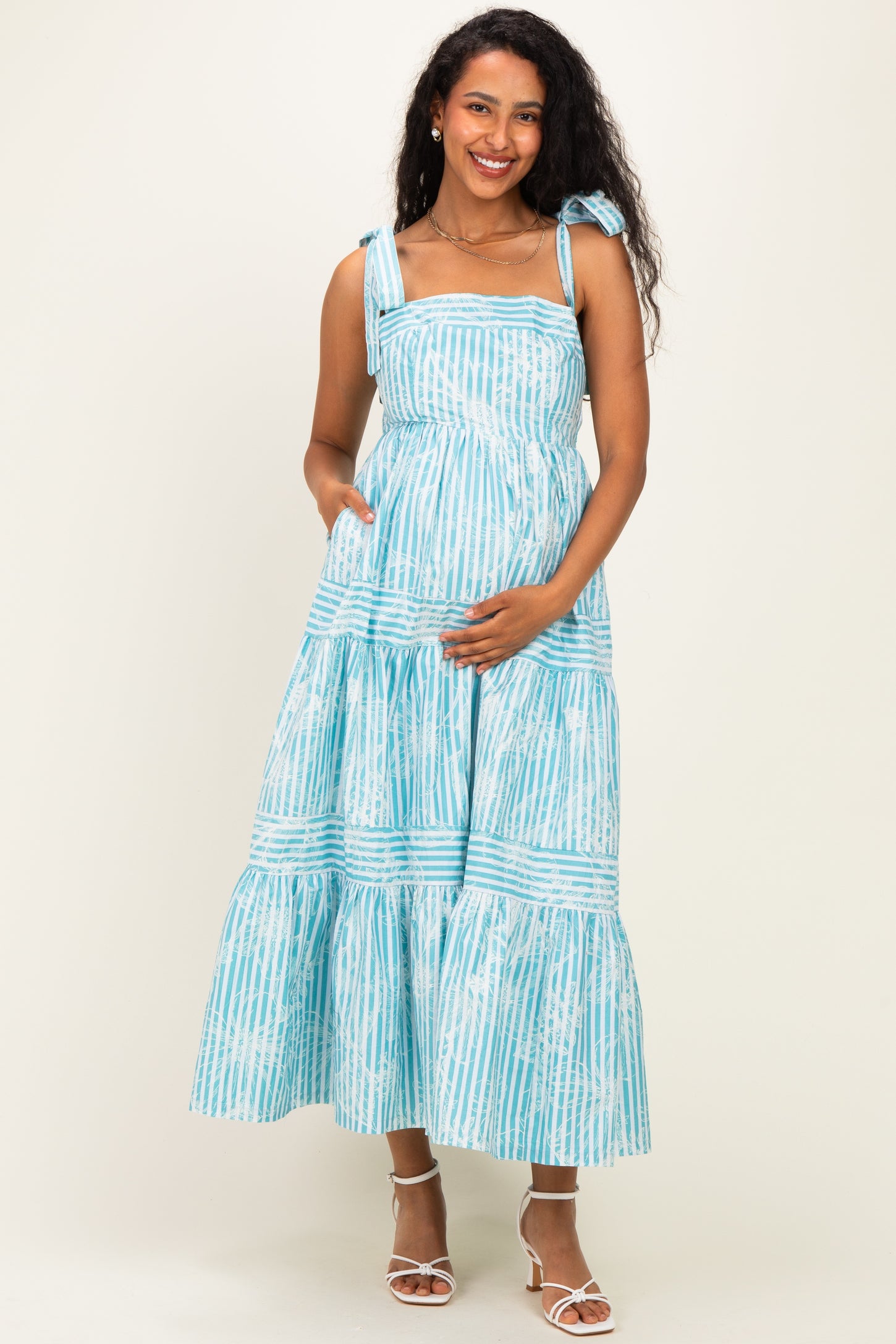 woman wearing a light blue maternity maxi dress with tie straps and a tiered skirt, holding her baby bump