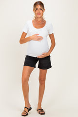 woman wearing a white short sleeve maternity top and black denim shorts, holding her baby bump