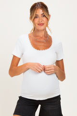 woman wearing a white maternity top with a scalloped neckline and short sleeves, showing her baby bump