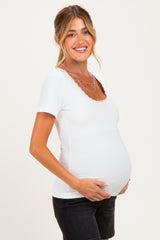 woman wearing a white scalloped neckline maternity top and holding her baby bump