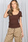 woman wearing a brown ribbed short sleeve top with a scalloped neckline and beige polka dot pants