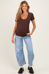 woman wearing a brown maternity ribbed t-shirt and blue wide-leg jeans, gently showing her baby bump
