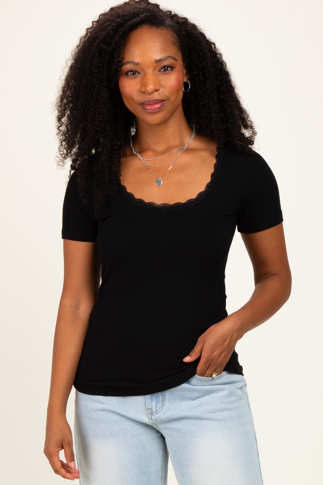 woman wearing a black ribbed short sleeve top with a scalloped neckline and light blue jeans