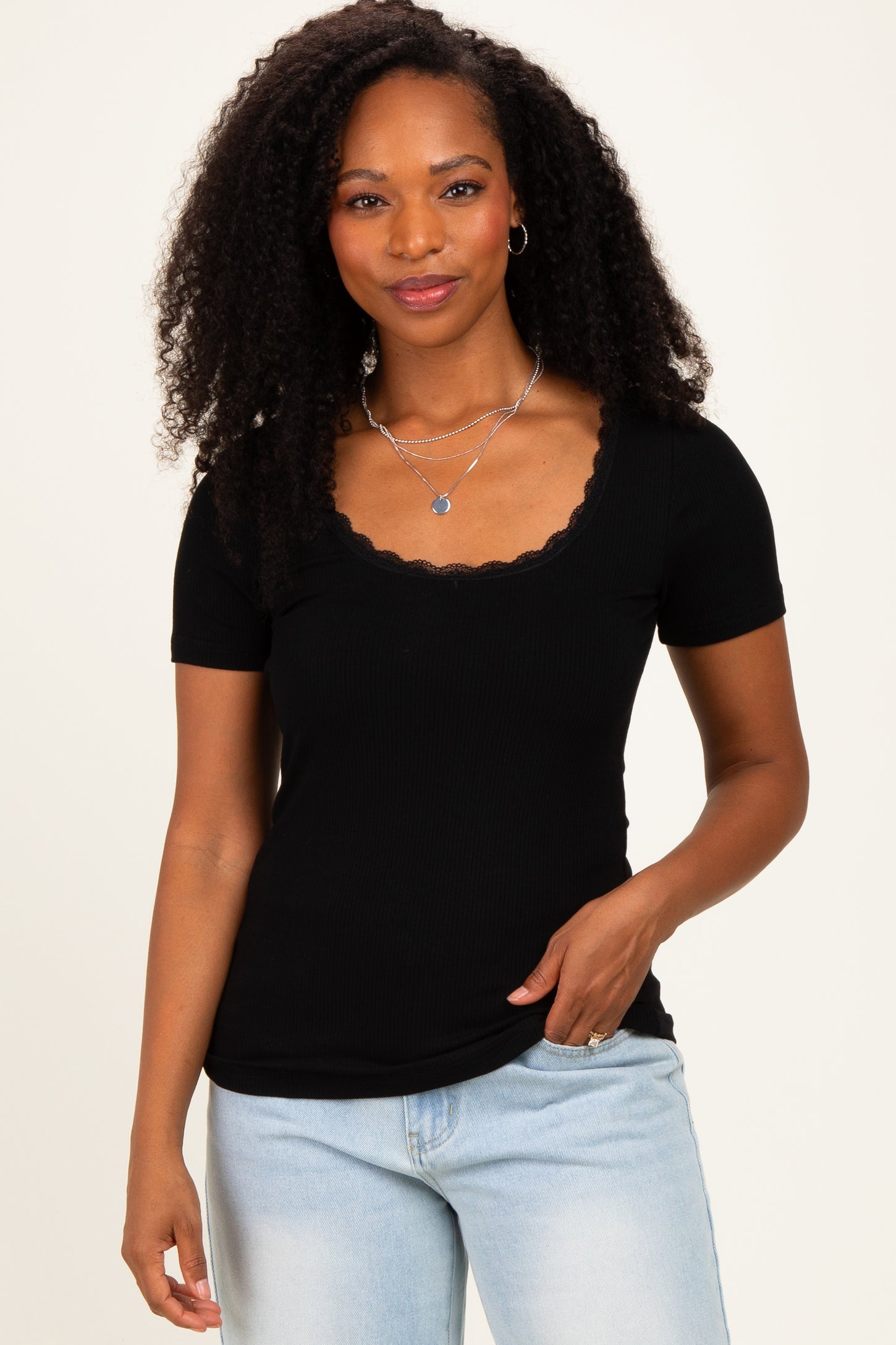 woman wearing a black ribbed short sleeve top with a scalloped neckline and light blue jeans