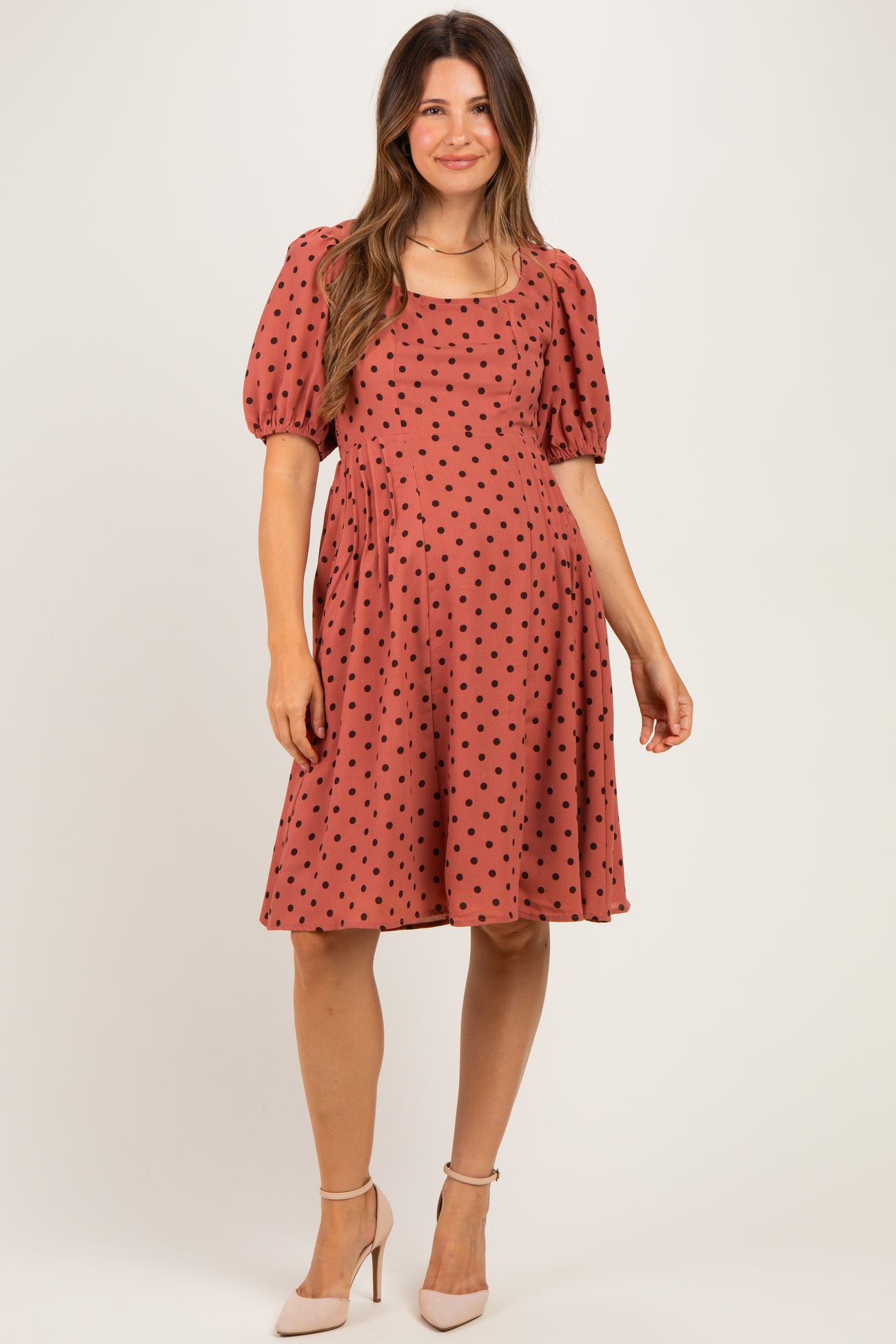 woman wearing a rust-colored maternity dress with black polka dots and puff sleeves