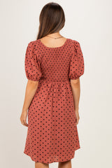 woman wearing a rust-colored maternity dress with puff sleeves and black polka dots, showing a smocked back design