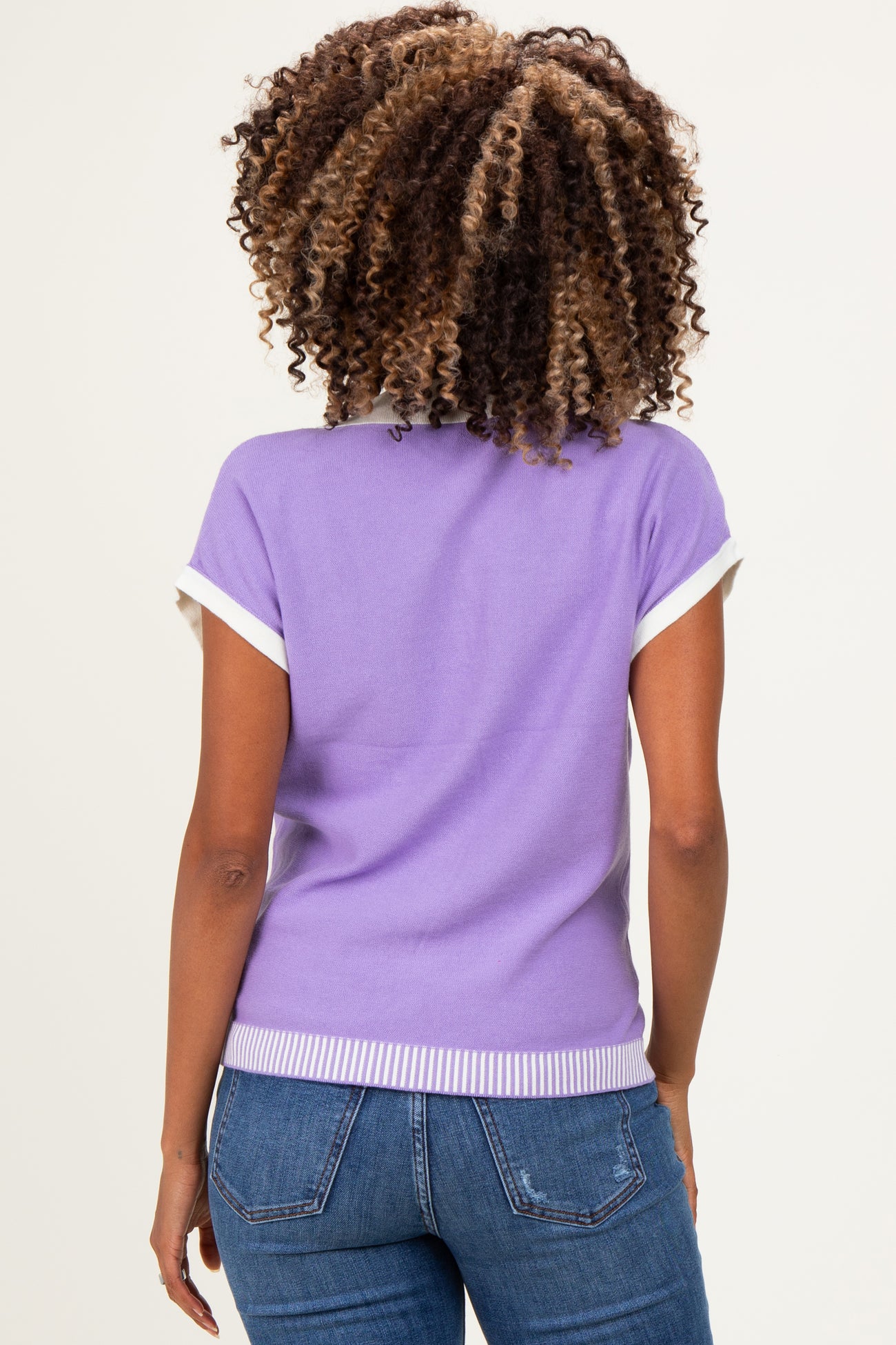 woman wearing a lavender short sleeve maternity top with white trim and back ribbed detail, paired with jeans