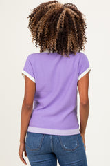 woman wearing a lavender short sleeve maternity top with white trim and back ribbed detail, paired with jeans