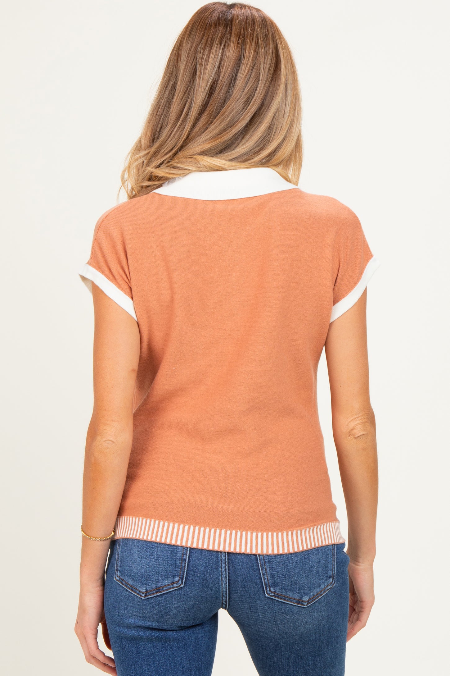 woman wearing a short sleeve rust-colored maternity polo with white collar and ribbed hem