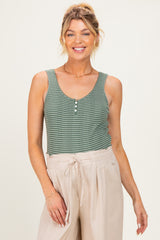 woman wearing a green checkered maternity tank top with buttons and light beige linen pants, smiling at the camera