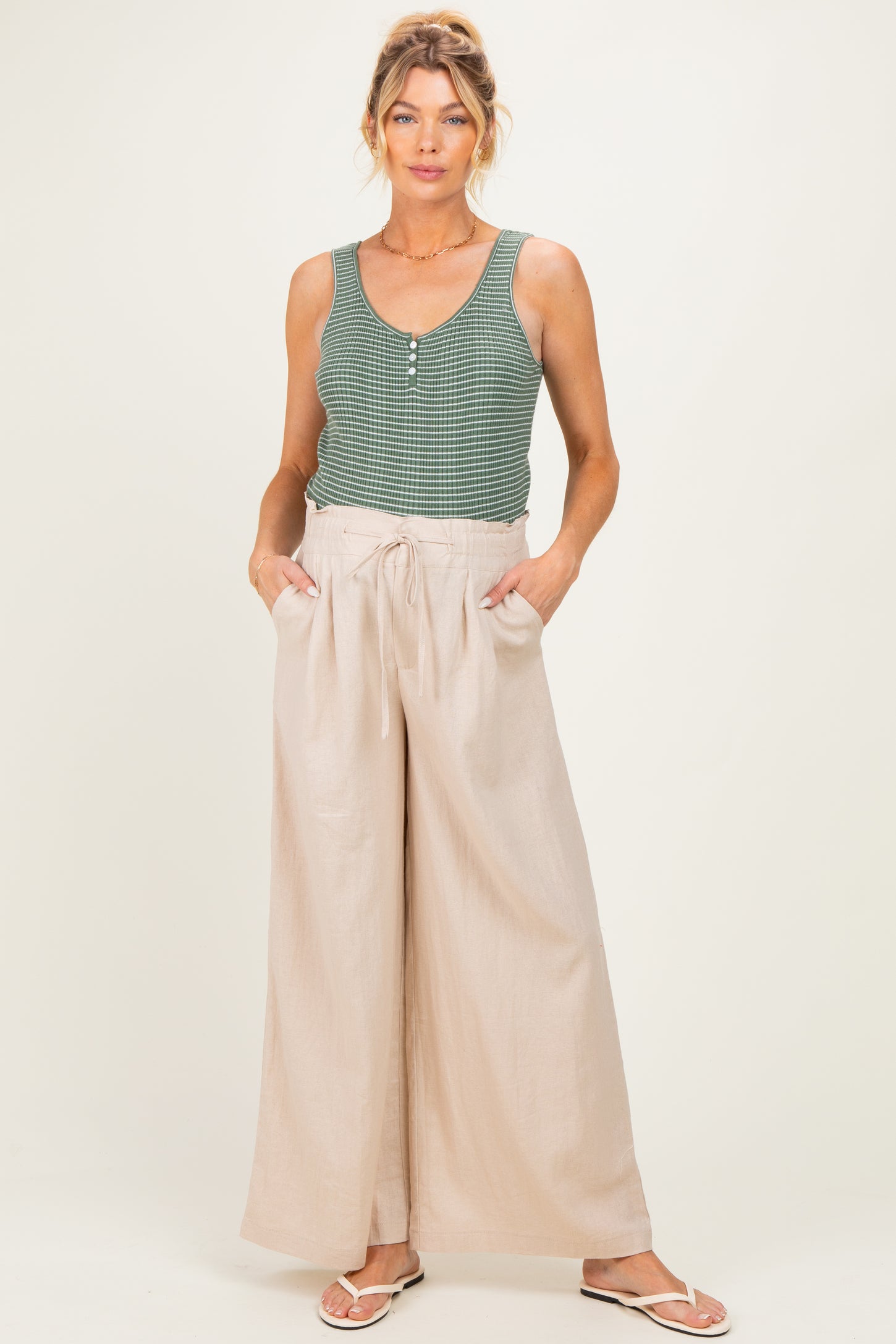 woman wearing a green sleeveless maternity top and beige wide-leg maternity pants with pockets