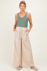 woman wearing a green sleeveless maternity top and beige wide-leg maternity pants with pockets