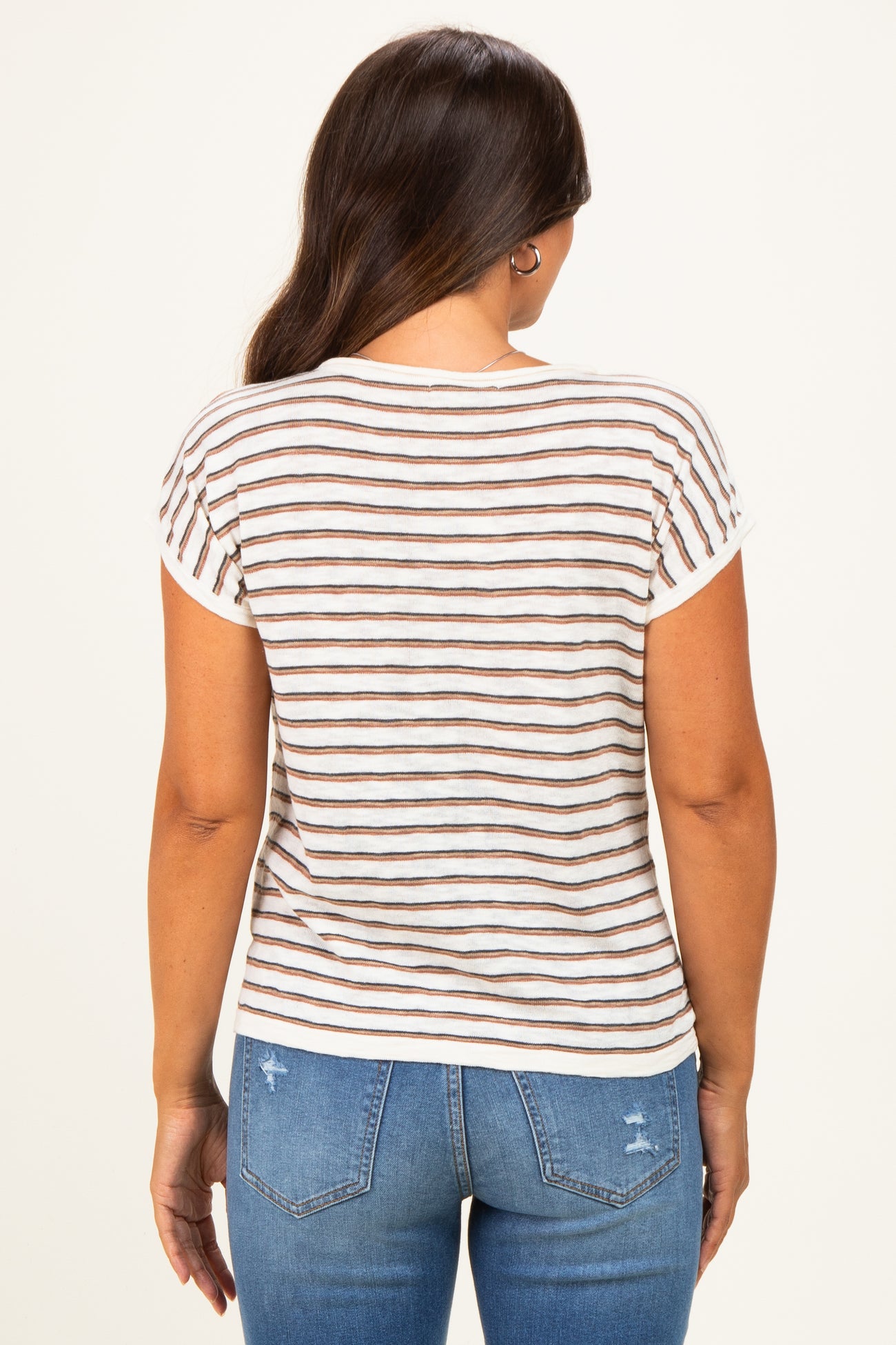 woman wearing a cream and brown striped maternity top seen from the back paired with light blue distressed jeans