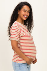 woman wearing a beige and red striped maternity top and gently holding her baby bump