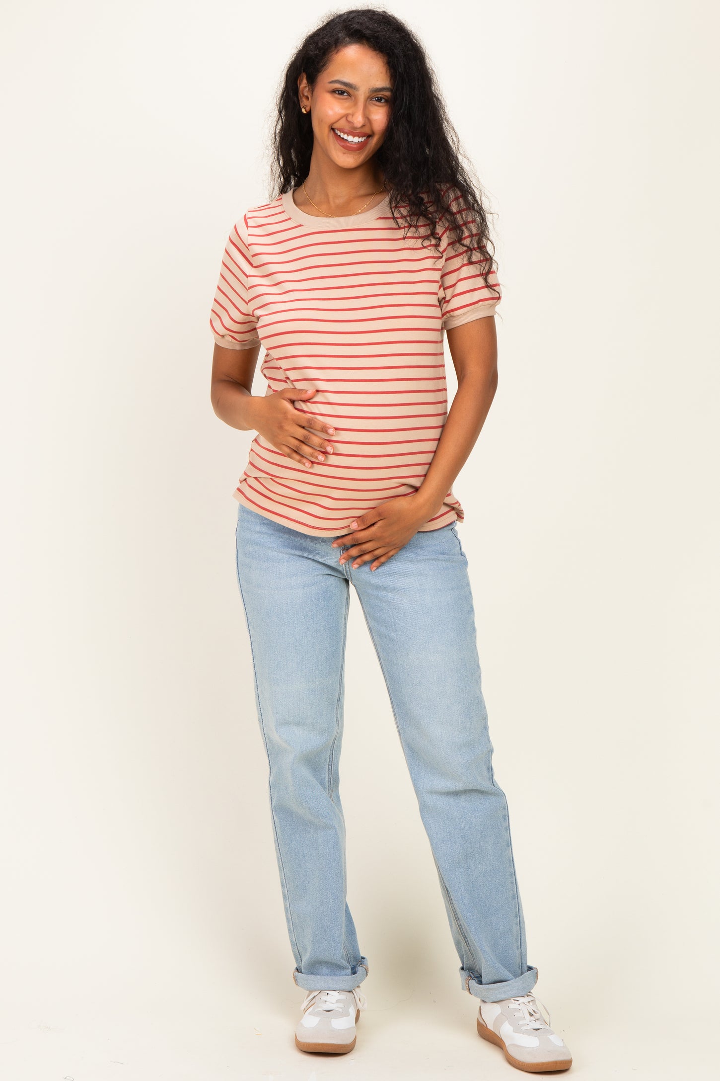 woman wearing a striped maternity t-shirt and light blue jeans, gently holding her baby bump