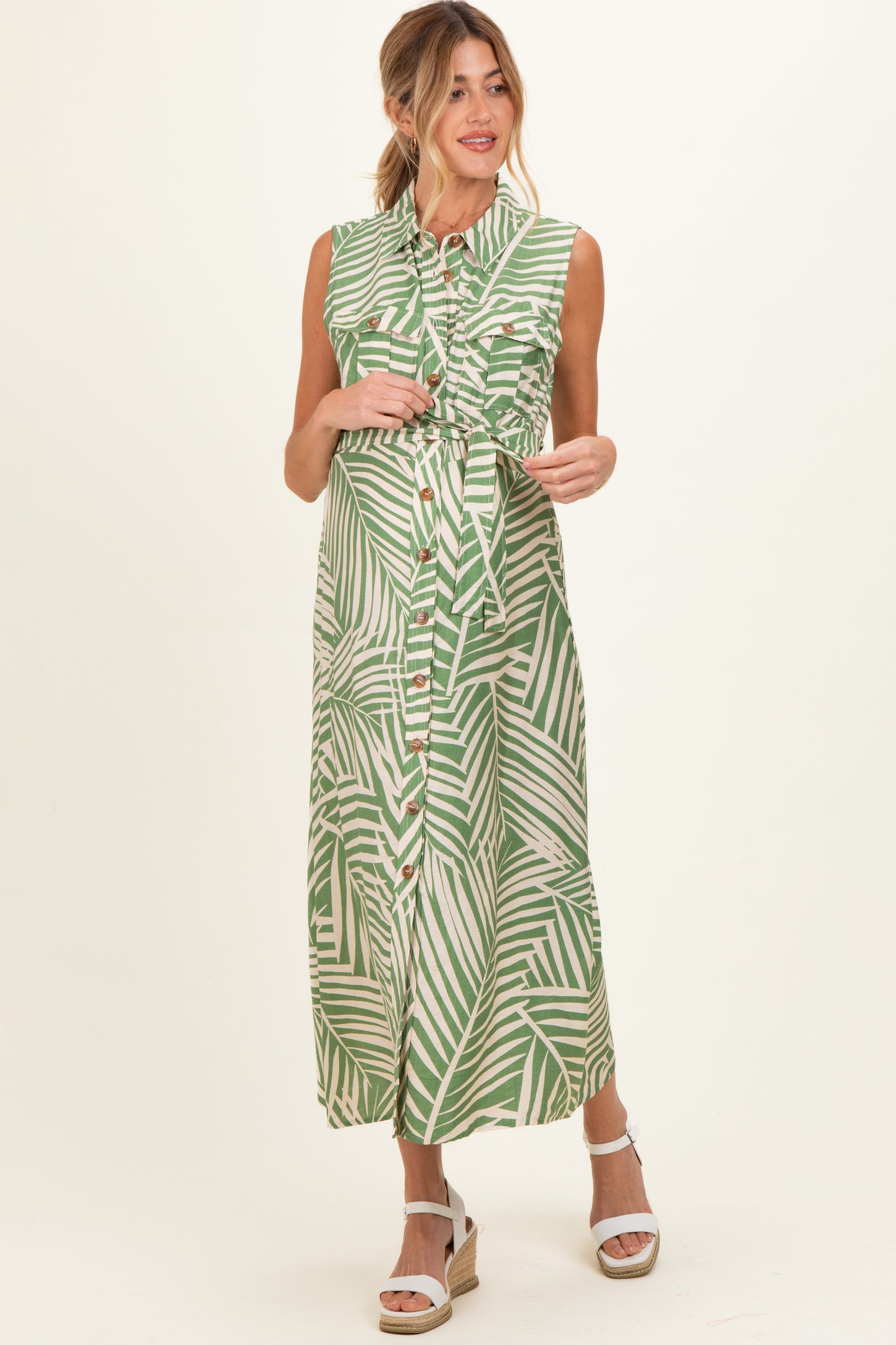 woman wearing a green palm leaf print maternity maxi dress with a fitted bodice and button-down front, holding her baby bump