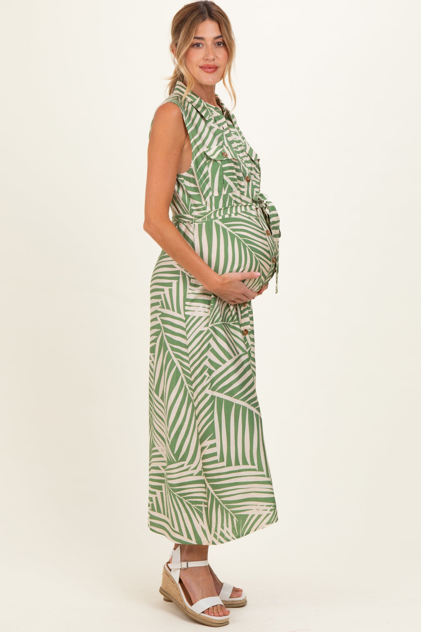 woman wearing a green and white tropical print maternity dress and holding her baby bump