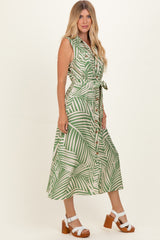 woman wearing a green and white palm print midi dress with a belted waist and buttons, standing on a neutral background