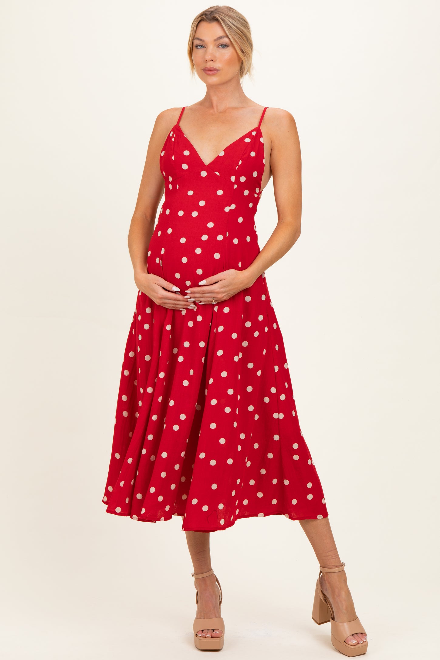woman wearing a red polka dot maternity dress and holding her baby bump